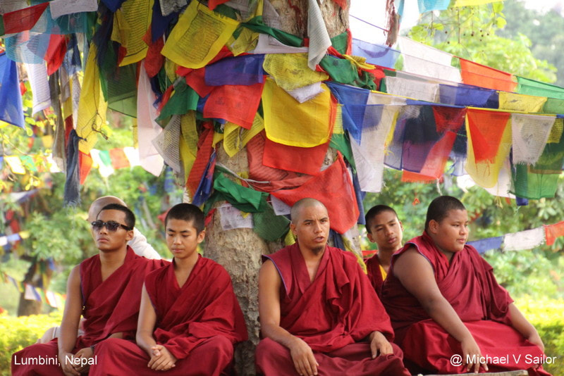 Buddhist monks sitting under tree and prayer flags in Nepal.