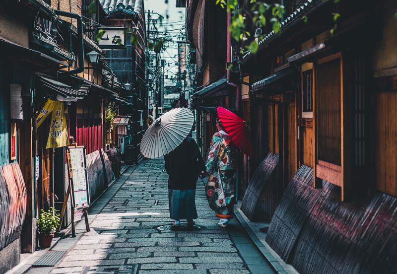 Two Japanese women in kimono walking on a narrow city street in Japan